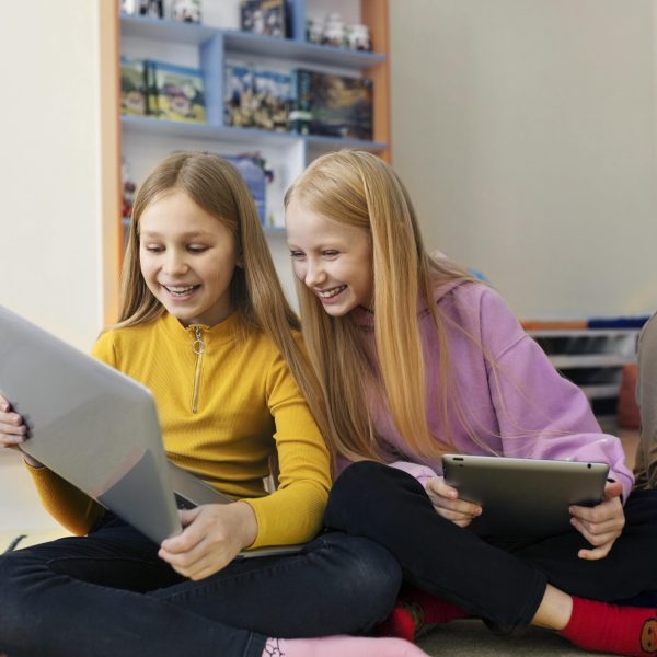 two-young-girls-working-together-using-their-laptop-tablet-min